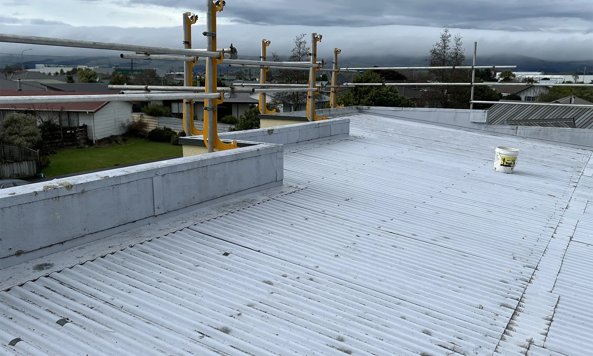 Image of an old corrugated steel roof in need of replacing. There is a scaffold at the back and the sky is grey and cloudy
